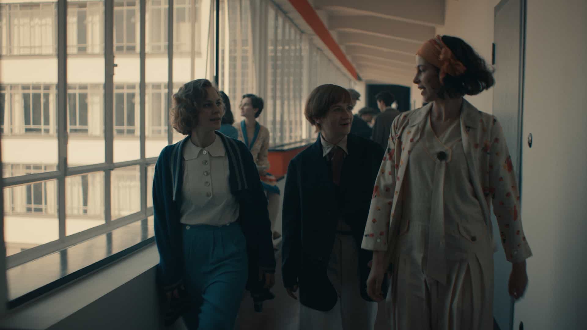 Filmszene. Lotte Brendel im Gespräch mit Anni Albers und Friedl Dicker, während sie einen lang Gang im Bauhaus Dessau entlanglaufen.